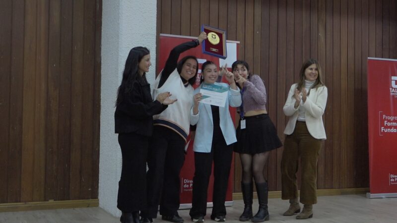 Grupo de estudiantes en un escenario recibiendo un reconocimiento del programa Impulsa; una de ellas levanta una placa mientras otra sostiene un certificado, acompañadas por personas que aplauden frente a un fondo institucional de la Universidad de Talca.