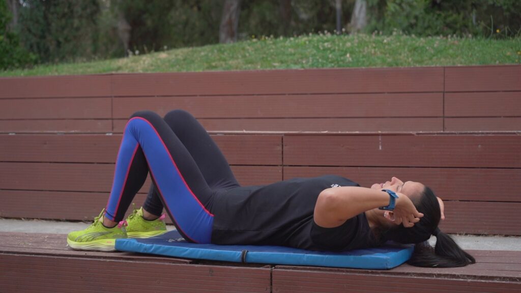 Mujer realizando ejercicios sobre una colchoneta azul al aire libre en el Parque Río Claro durante la grabación del programa En Rutina.