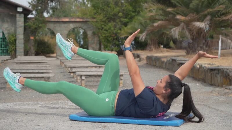 ersona realizando un ejercicio de fortalecimiento abdominal con una pelota medicinal durante una rutina de entrenamiento físico al aire libre.